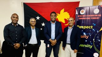 Four men in business attire standing in front of the Papua New Guinea flag