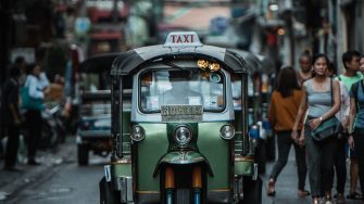 A tuk tuk (peddi cab) is heading towards the camera down a street.