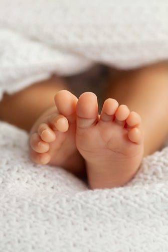 Adorable baby feet covered in a white blanket, maternity and babyhood concept - Image