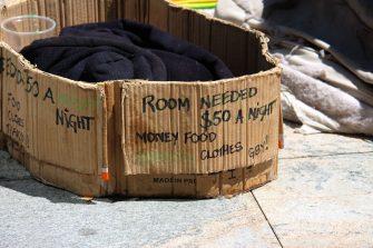 Collection cup and cardboard signage of a homeless man. North Sydney