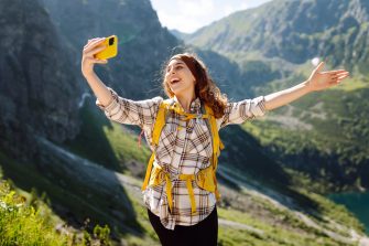 Positive tourist woman taking picture outdoors for memories, making selfie with valley mountains view, sharing travel adventure journey. Lifestyle, travel, tourism, active life.