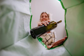 An image from inside green recycling bag of woman throwing a glass bottle to recycle