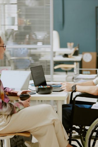 Two Caucasian coworkers having nice conversation while female colleague drinking coffee and her male colleague with disability coding