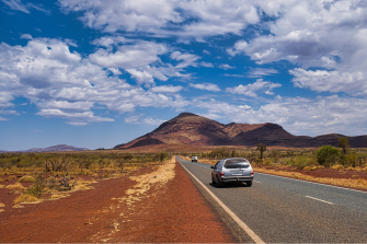 A station wagon travels on a long mostly empty road in outback Australia