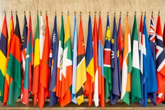 Some world national flags on poles on a wall.