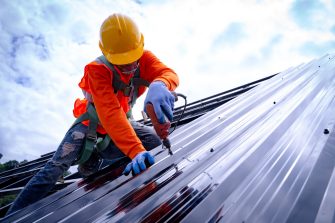 Roofer working on roof structure of building on construction site,Roofer using air or pneumatic nail gun and installing Metal Sheet on top new roof.