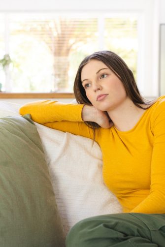 Portrait of thoughtful caucasian woman sitting on couch on in living room at home, copy space