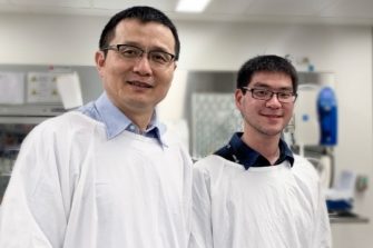 Two research students in lab coats smiling at the camera