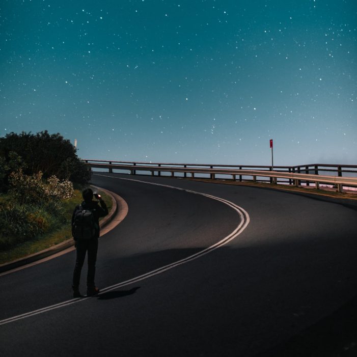 Man standing in the middle of the road looking at night sky