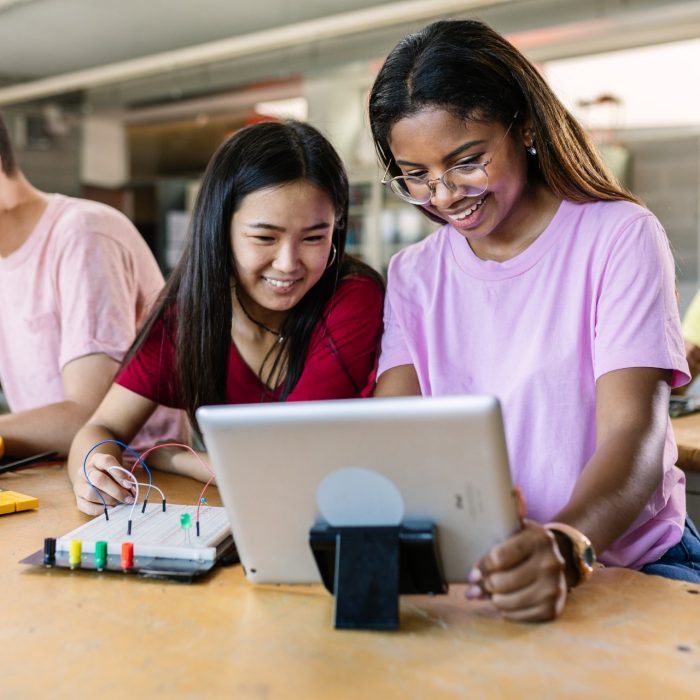 Group of diverse teenage students learning together to build electronic circuits at high school - Asian and african american female classmate working at technology class