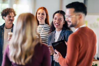 Happy diverse colleagues have fun at lunch break in office, smiling multiracial employees laugh and talk  drinking coffee