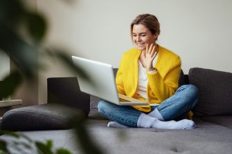 Young happy woman waving into laptop camera during online conversation by video call at home