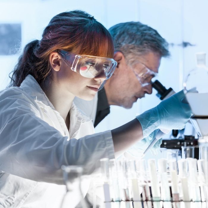 Health care researchers working in life science laboratory. Young female research scientist and senior male supervisor preparing and analyzing microscope slides in research lab.