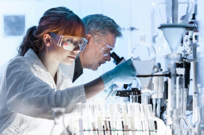 Health care researchers working in life science laboratory. Young female research scientist and senior male supervisor preparing and analyzing microscope slides in research lab.