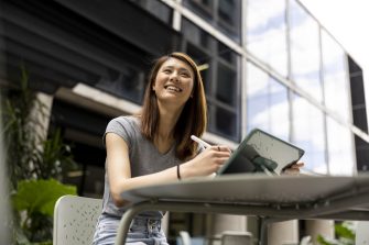 Young female student using iPad and pen in open air courtyard