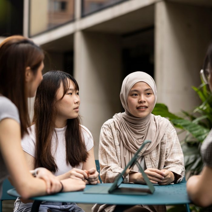 4 Students in courtyard sitting at table with ipad