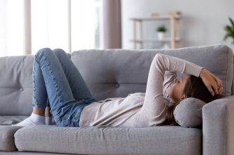 Depressed young person lying on couch at home sufering from fatigue