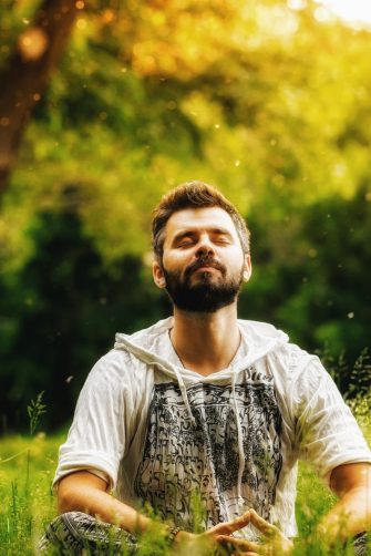 A bearded person meditating on green grass in the park