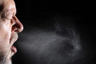 Close-up of a man's face in profile sneezing showing droplet cloud