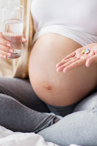 Close up of pregnant person sitting in bed at home with pills and glass of water
