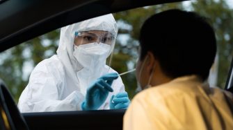 Health professional in PPE suit  giving nasal swab to person in car for   coronavirus(covid-19) PCR test 
