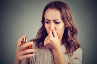 A woman holds her nose in disgust while looking at a beautiful jar of perfume.