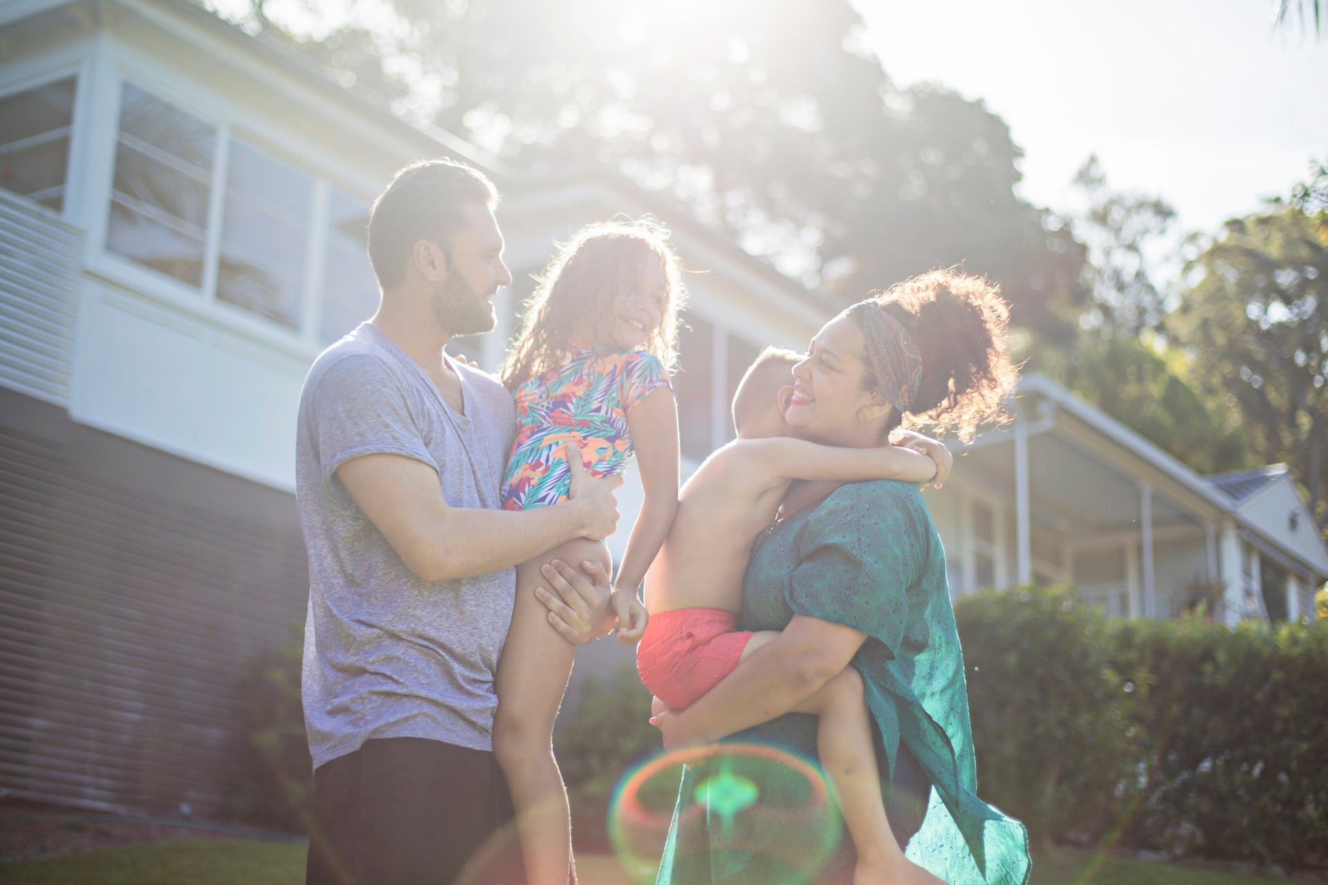 A couple stand holding their young kids in the garden.