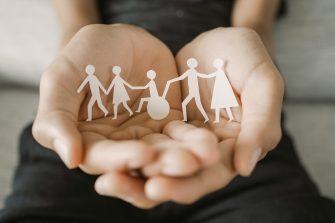 hand holding paper cut-out of people holding hands, one of them in a wheelchair