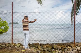 A man standing at a fence overlooking water on Manus Island