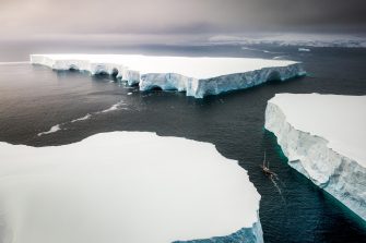 Aerial view of a large iceberg floating near an ice shelf under grey skies 0