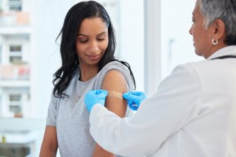 Healthcare, woman and doctor with plaster, vaccination and consultation in a hospital, cure and disease. Female patient, client and medical professional with care, vaccine and injection for safety.