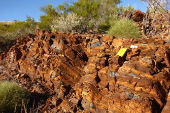 An orange rock wall with some black, shiny rocks at a geological site in the Australian desert