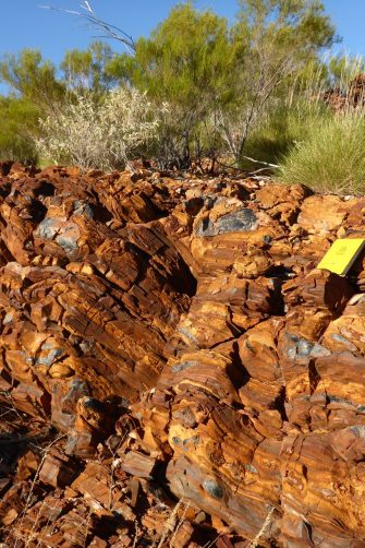 An orange rock wall with some black, shiny rocks at a geological site in the Australian desert