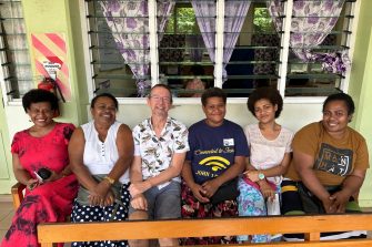 A man sitting with five women outside a building.