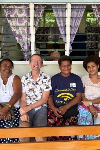 A man sitting with five women outside a building.