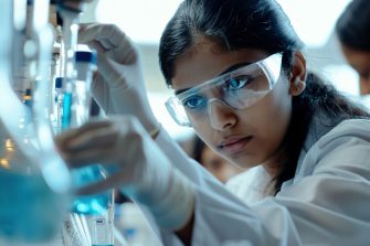 Female scientist working in a laboratory holding test tube, taking a mixed liquid from a flask. Woman wearing a white lab coat and safety glasses making medical experiment. Science technology project