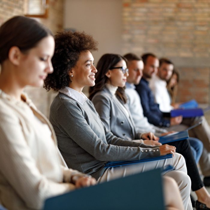 Large group of people sitting in waiting room before job interview for their potential business position. Focus is on happy black woman.