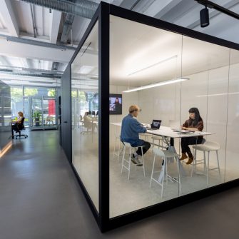 Businesspeople sitting in a small cubicle in hybrid office. Man and woman working on laptop in a box cubicle.