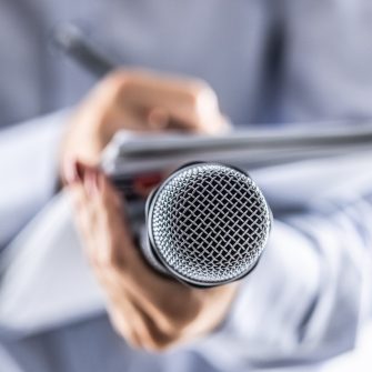 A journalist holds a microphone at a press conference and writes information in a notebook