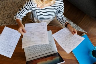 Mature woman with documents using laptop at home