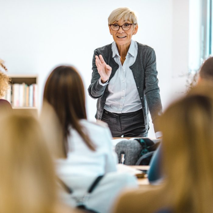 Happy senior teacher talking to large group of univerity students in amphitheater