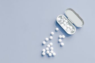 Woman in casual clothing handling a pill blister pack with a focus on hand movements and a glass of water in the background.