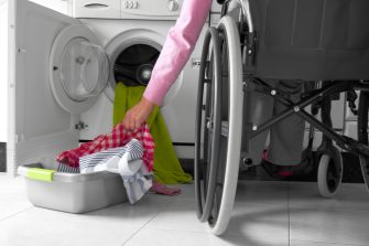 Woman in a wheelchair putting clothes in her washing machine.