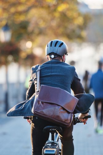 A rear view of a businessman commuter with electric bicycle traveling to work in city. Copy space.