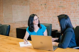 Two women sitting at table with laptop, talking