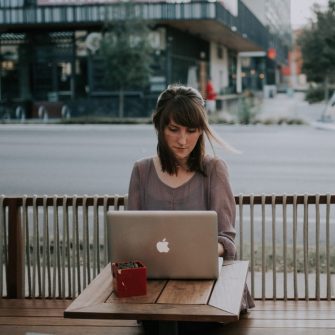 Young woman sitting at outdoor cafe table with laptop