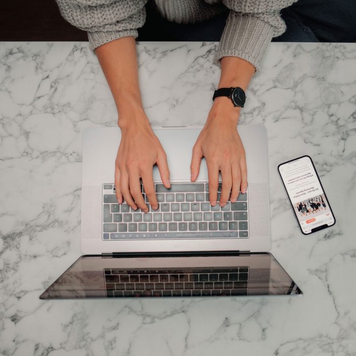 Photo of person typing from above, laptop and phone in view