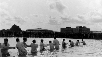 archive image of team of men pulling a rope together through a water