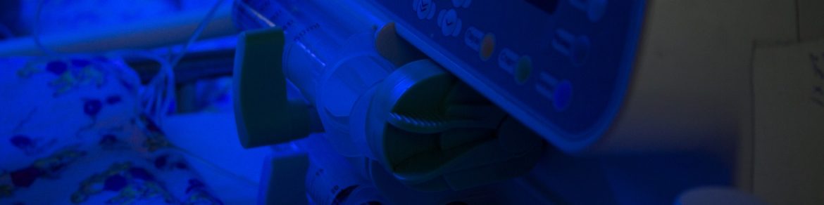 Newborn baby under blue UV light for phototheraphy on infant warmer in neonatal intensive care unit. Child baby having a treatment for jaundice under ultraviolet light in incubator. Device for delivery of a dropper.