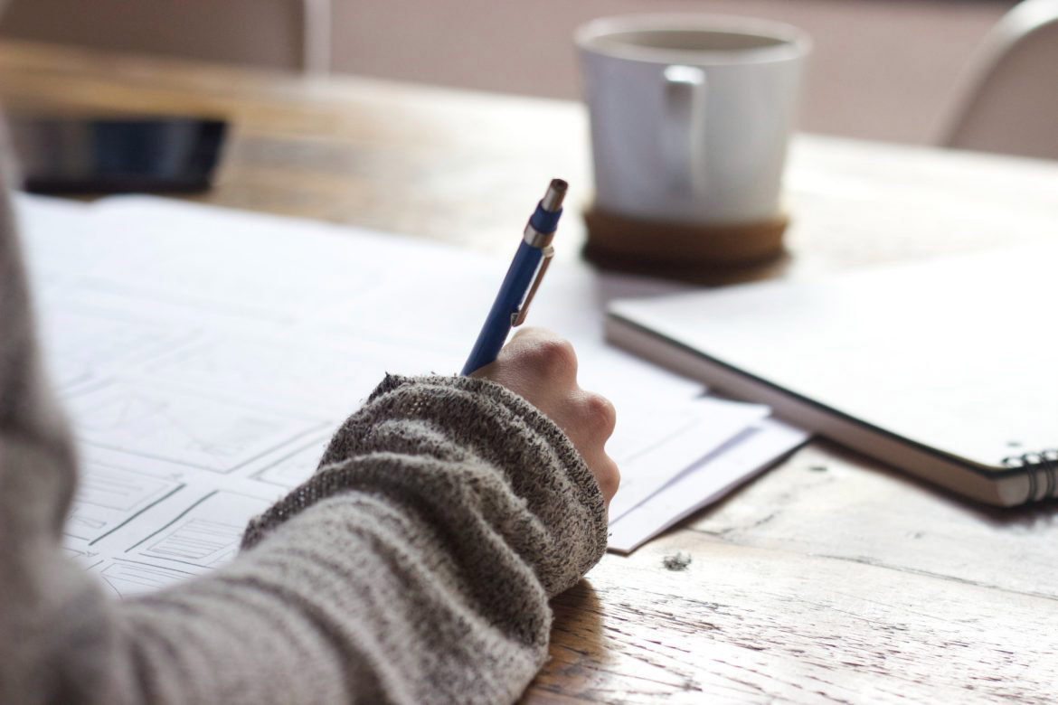 Picture of person signing documents with coffee cup in the background